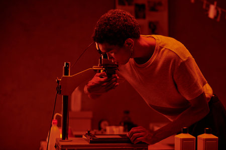 A meticulous photographer inspecting photo negative under the red safety light of a darkroom