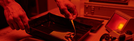 banner of photographer taking freshly developed photo paper in chemical solution with tweezers