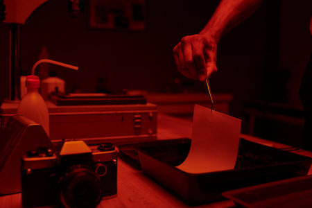 cropped shot of young man delicately immerses photo paper in a darkroom bath with chemicalsの写真素材