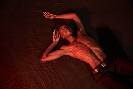 sexy african american man lying topless on water with closed eyes, dark lights, fashion concept
