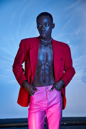 fashionable african american man in pink pants and red blazer looking away on watery backdrop