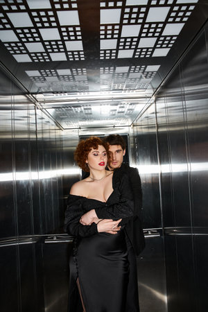 tempting loving boyfriend and girlfriend in elegant black attires hugging in elevator, sexy couple