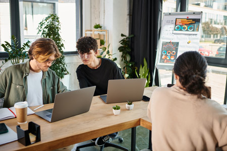 Young professionals in their 20s sharing ideas near laptops in a coworking space, blurred foreground