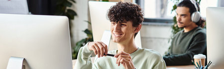 satisfied curly man engaged in retouching work, holding stylus pen and looking at monitor, banner
