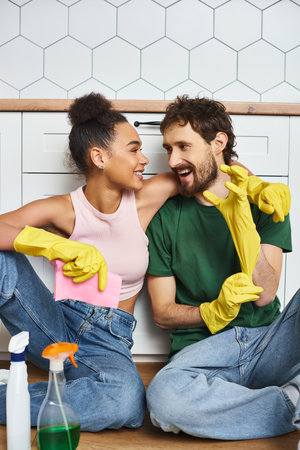 loving cheerful multicultural couple in comfy homewear sitting on floor during spring cleaningの写真素材