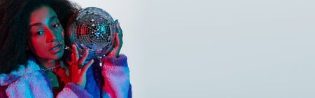 appealing african american woman in faux fur posing with disco ball and looking at camera, banner
