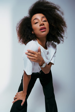 appealing african american woman in chic attire with curly hair looking at camera, fashion concept