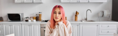appealing young pink haired woman in comfy homewear looking at camera while in kitchen at homeの写真素材