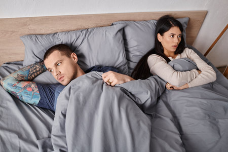 high angle view of young interracial offended couple lying down on bed at home, relationship troubleの写真素材
