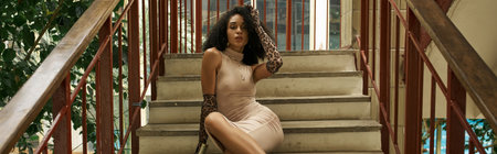 young black woman in dress and animal print gloves sitting on stairs in urban setting, bannerの写真素材