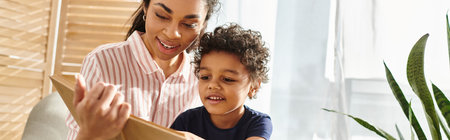 merry appealing african american woman in cozy attire reading book to her little son at home, bannerの写真素材