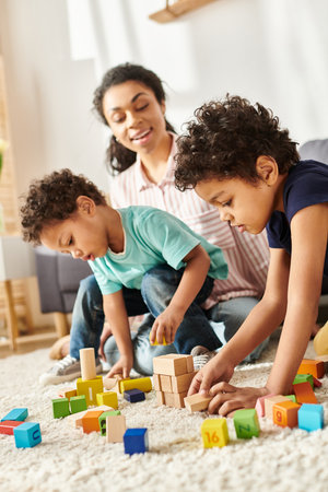 good looking merry african american mother in cozy homewear playing with toys with her adorable sonsの写真素材