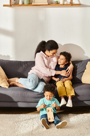 joyous african american mother sitting watching movies with her adorable sons in living room at homeの写真素材