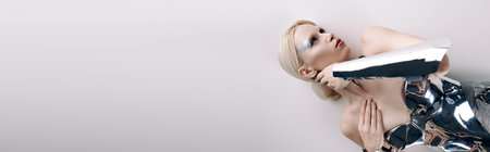 beautiful bizarre woman with blonde hair in silver futuristic attire lying on floor, bannerの写真素材