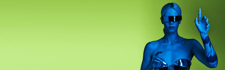 peculiar woman in robotic attire with sci fi sunglasses posing in lights on green backdrop, bannerの写真素材