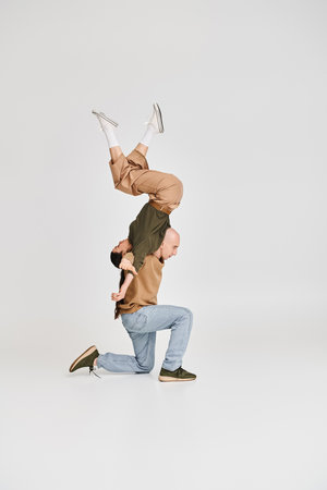 brunette woman balancing upside down with support of man in casual attire while rehearsing in studio