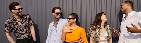 jolly interracial friends in vivid clothing talking to each other happily and posing by wall, banner