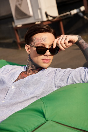 attractive young man in casual outfit with tattoos and stylish sunglasses posing on rooftopの写真素材
