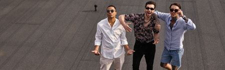 interracial jolly male friends with sunglasses posing on rooftop and looking at camera, banner