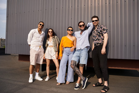 group of joyous multicultural friends in vibrant clothes posing by wall and smiling at camera