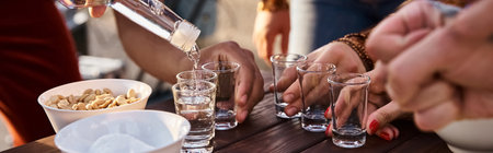 cropped view of interracial young friends pouring tequila shots while at rooftop party, banner