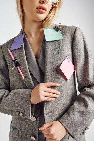 cropped view of young elegant woman wearing stylish suit with stationery on it on gray backdrop