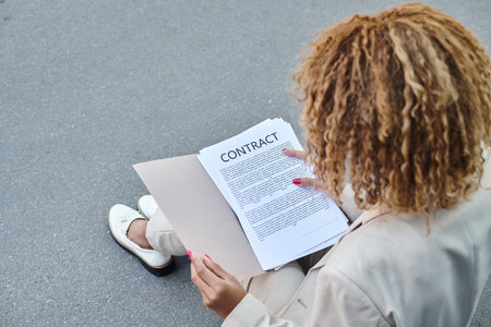 overhead view of african american curly businesswoman reviewing contract on the go outdoors