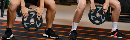 cropped view of athletic women in cozy sportwear squatting with weight plates while in gym, banner