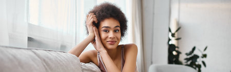 portrait of young and curly african american woman in lingerie looking at camera at home, banner