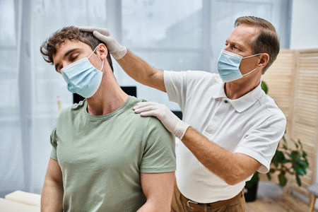 good looking mature doctor with mask and gloves helping his patient to rehabilitate in hospitalの写真素材