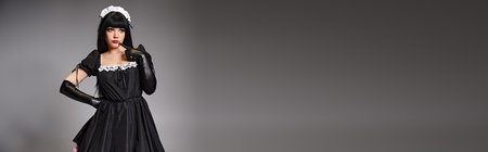 sexy appealing cosplayer in maid costume posing alluringly and looking away on gray backdropの写真素材