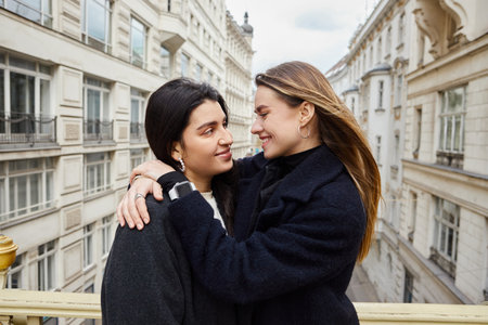 Intimate moment on balcony with city architecture view as backdrop, cheerful lesbian women in loveの写真素材