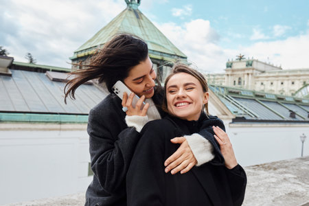 happy lesbian woman talking on smartphone and hugging her girlfriend during trip to Viennaの写真素材
