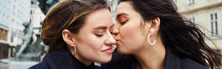 happy lesbian woman kissing in cheek her girlfriend by a fountain statue in Vienna, bannerの写真素材