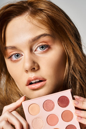 Closeup beauty shot of woman with peach makeup palette near face on grey background