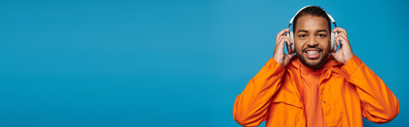 banner of african american man in orange outfit look to camera and hold with hands on headphonesの写真素材