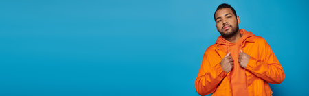 horizontal shot of attractive african american young man in orange outfit on blue backgroundの写真素材