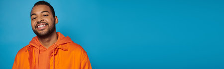 banner of happy african american man in his 20s smiling broadly with leaning head on blue backgroundの写真素材