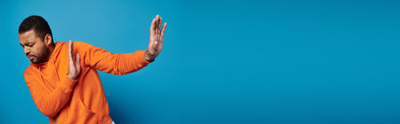 banner of african american man in vibrant outfit with closed eyes refusing and hiding behind handsの写真素材