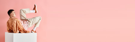 Side view photo of man in peach outfit lying on white cube with leg up on pink background, bannerの写真素材