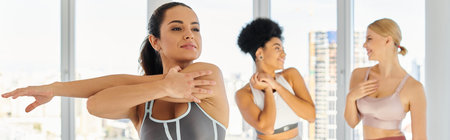 young woman in sportswear stretching before pilates class next to interracial female friends, banner