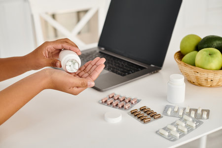 cropped view of african american nutritionist pouring pills into hand palm from medication bottleの写真素材
