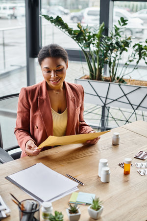 happy african american dietitian reviewing envelope near supplements on her working deskの写真素材