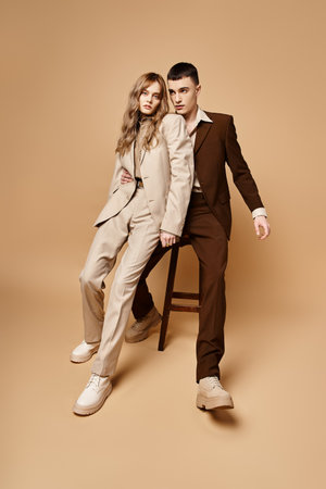 appealing young woman in pastel suit looking at camera next to her handsome boyfriend on chairの写真素材