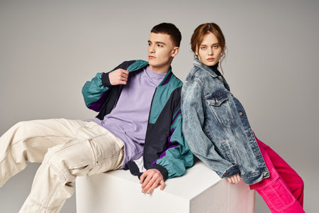 beautiful woman in fashionable bomber looking at camera next to her handsome boyfriend on white cube