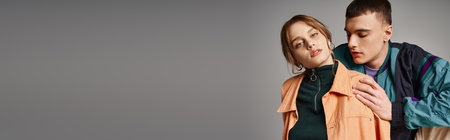 pretty woman in bomber looking at camera next to her handsome boyfriend on gray backdrop, bannerの写真素材