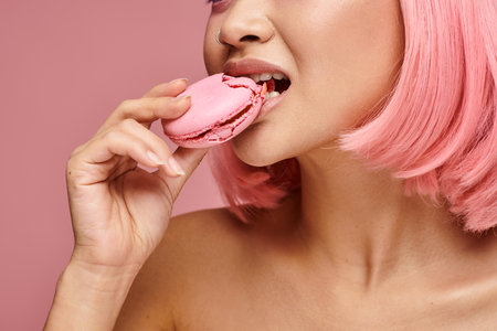 cropped shot of young woman with pink hair eating macaroon against vibrant backgroundの写真素材