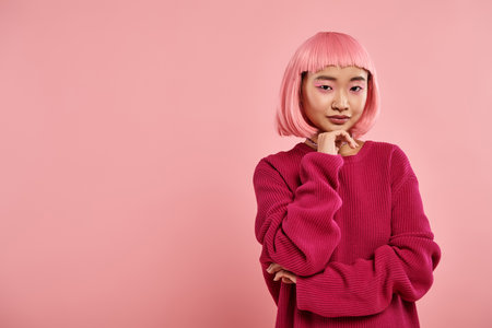 confident asian girl with pink hair in big jumper supporting chin with hand on vibrant backgroundの写真素材