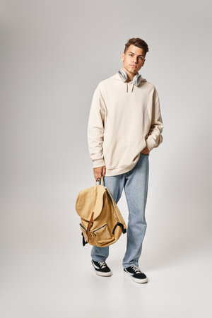 handsome student in headphones and casual outfit walking with backpack against grey backgroundの写真素材
