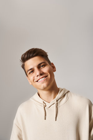 portrait of smiling young man with brown hair and grey eyes leaning head against light backgroundの写真素材